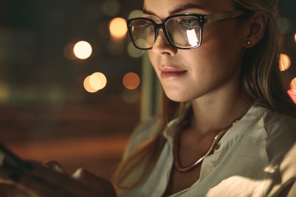 Close up of young woman wearing glasses using cellphone in office. Businesswoman texting on her smart phone.