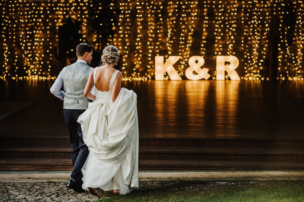 Young couple at their wedding walking towards a reception full of lights and LED Neon signage